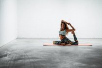 Side view of fit female in sportswear sitting on mat and practicing yoga in Eka Pada Rajakapotasana with mudra gesture — Stock Photo