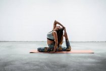 Вид сбоку сидящей на коврике и практикующей йогу Эка Пада Раджакапотасана с жестом мудра — стоковое фото