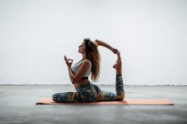 Seitenansicht einer fitten Frau in Sportbekleidung, die auf einer Matte sitzt und Yoga in Eka Pada Rajakapotasana mit Mudra-Geste praktiziert — Stockfoto