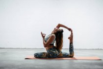 Vista laterale della vestibilità femminile in abbigliamento sportivo seduta su tappetino e praticare yoga in Eka Pada Rajakapotasana con gesto mudra — Foto stock