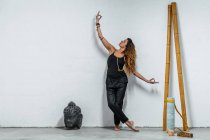 Femme tranquille en vêtements de sport debout avec les bras tendus et geste mudra tout en regardant dans la chambre avec tapis de yoga tordu et tête de Bouddha — Photo de stock