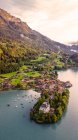 Desde arriba vista del dron de la pequeña península con el antiguo castillo de Iseltwald y pueblo situado en la orilla del lago en terreno montañoso en Suiza al atardecer en la noche de verano - foto de stock