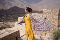 Monumentale edificio antico con remoto turista donna che esce dalla porta in abito giallo mentre si gode una calda giornata di sole nel villaggio di marmo di Al Bahah — Foto stock