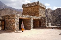 Bâtiment ancien monumental avec une touriste féminine éloignée sortant de la porte en robe jaune tout en profitant d'une chaude journée ensoleillée dans le village de marbre à Al Bahah — Photo de stock
