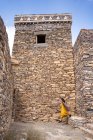 Distanzierte Frau in bunten Kleidern spaziert zwischen schäbigen antiken Mauern historischer Gebäude des Marmordorfes Al Bahah in den Bergen Saudi Arabiens — Stockfoto