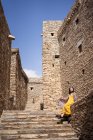 Von unten ein monumentales antikes Gebäude, in dem abgelegene Touristinnen in gelbem Kleid aus der Tür kommen, während sie den heißen, sonnigen Tag im Marmordorf Al Bahah genießen — Stockfoto