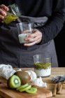 Tiro cortado de mulher em avental preparando iogurte com purê de kiwi fresco — Fotografia de Stock