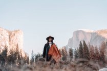Glücklich entspannte junge Reisende in stylischem Outfit sitzt auf einer Steinumrandung vor malerischer Berglandschaft mit felsigen Klippen und Nadelwald im Yosemite Nationalpark in den USA — Stockfoto