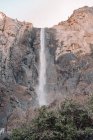 A partir de baixo vista incrível de poderosa cachoeira fluindo de alta penhasco rochoso contra céu sem nuvens em dia ensolarado no Parque Nacional de Yosemite, nos EUA — Fotografia de Stock