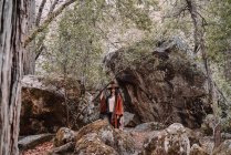 Junge Wanderin in stylischer Boho-Kleidung und Hut steht zwischen riesigen Felsbrocken im Wald während einer Reise zum Yosemite-Nationalpark in Kalifornien — Stockfoto
