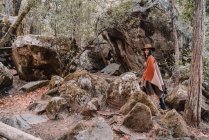 Jeune randonneuse en boho élégant et chapeau debout parmi les rochers géants dans la forêt pendant le voyage au parc national de Yosemite en Californie — Photo de stock