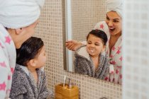 Menino bonito em roupão de banho e mãe sorridente em turbante toalha de pé no banheiro e escovação de dentes — Fotografia de Stock