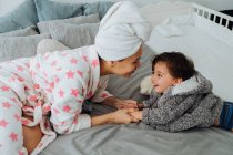 Веселая женщина в халате веселится с маленьким мальчиком на мягкой кровати, смотрящим друг на друга — стоковое фото