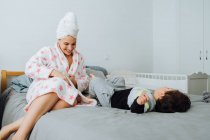 Cheerful woman in bathrobe dressing up little son while playing together at home looking at each other — Stock Photo