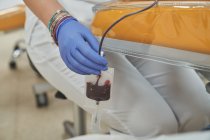 Mujer especialista en guantes de látex que realiza la inyección con jeringa al paciente anónimo durante el procedimiento de transfusión de sangre en el hospital - foto de stock