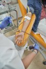 Сверху урожая кормилица в защитных перчатках с мешком крови в руке, работающая с пациентом во время процедуры сдачи крови в современном медицинском центре — стоковое фото