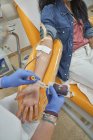 De arriba de la cosecha la enfermera en los guantes protectores con la bolsa de la sangre en la mano que trabaja con el paciente durante el procedimiento de la donación de sangre en el centro médico moderno - foto de stock
