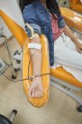 Вид з боку низького кута молодої жінки в захисній масці перегляду смартфона під час процедури переливання крові в лікарні — стокове фото