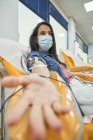 Visão lateral da jovem mulher em máscara protetora sentada em poltrona médica durante o procedimento de transfusão de sangue no hospital contemporâneo — Fotografia de Stock