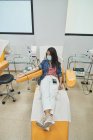 Женщина в защитной маске сидит в медицинском кресле во время процедуры переливания крови в современной больнице — стоковое фото