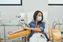 Женщина-донор с нашивкой под рукой, сидящая в медицинском кресле после процедуры переливания крови — стоковое фото