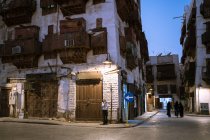 Typische Wohngebäude aus Stein mit schäbigen Mauern und Balkonen auf einer alten Straße der Stadt Dschidda in Saudi-Arabien bei Nacht mit spazierenden Menschen — Stockfoto
