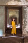 Full body young Asian female in traditional saffron dress standing in corridor of old abandoned stone house in Jeddah city in Saudi Arabia — Stock Photo