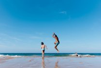 Back view of unrecognizable man with little son running and jumping into sea water while having fun together during summer holidays on sandy beach — Stock Photo
