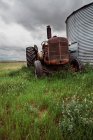 Low angle of rusty agricultural machine with huge wheels parked on green lawn near barn in countryside — Stock Photo
