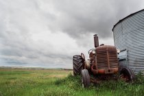 Baixo ângulo de máquina agrícola enferrujada com rodas enormes estacionadas no gramado verde perto do celeiro no campo — Fotografia de Stock
