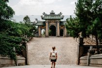 Von oben Seitenansicht einer entzückten Reisenden mit Rucksack, die im tropischen Garten in der Nähe religiöser Tempel spaziert und majestätische Landschaft genießt — Stockfoto