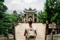 Von oben Seitenansicht einer entzückten Reisenden mit Rucksack, die im tropischen Garten in der Nähe religiöser Tempel spaziert und majestätische Landschaft genießt — Stockfoto