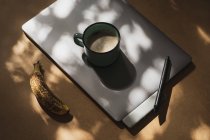 Kaffeebecher auf Grafik-Tablet mit Stift und reifer Banane im Sonnenlicht — Stockfoto
