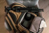 Draufsicht auf Tasche mit modernem Fotozubehör und weißer Atemschutzmaske auf Stuhl im Zimmer — Stockfoto