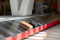 Metal baggage conveyor belt with suitcases near red emergency button at empty airport terminal — Stock Photo