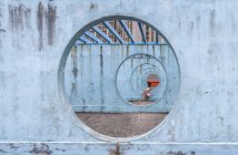 Frau im Sommerkleid sitzt auf Betonsockel einer ungewöhnlichen Stadtinstallation in Form eines Durchgangs mit runden Löchern und schaut weg — Stockfoto