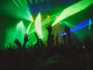 Back view silhouettes of people against illuminated with lights stage during music performance — Stock Photo