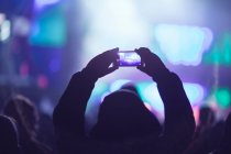 Silhouette einer nicht wiederzuerkennenden Person, die ein Video mit dem Smartphone aufnimmt, während sie moderne Show gegen beleuchtete Neon-Bühne anschaut — Stockfoto