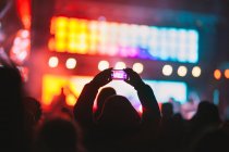 La silhouette della vista posteriore di una persona irriconoscibile che scatta video con smartphone mentre guarda lo spettacolo moderno contro il palco illuminato al neon — Foto stock
