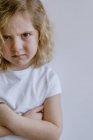 Enttäuschtes kleines Kind in lässigem T-Shirt blickt im Studio in die Kamera auf weißem Hintergrund — Stockfoto
