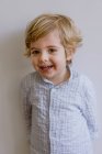 Очаровательный маленький ребенок в повседневной рубашке улыбается и смотрит в камеру на белом фоне студии — стоковое фото