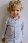 Petit enfant déçu en chemise décontractée debout près du mur blanc et pleurant sur fond blanc en studio — Photo de stock