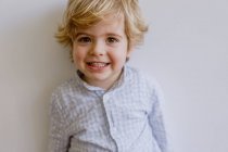 Criança adorável vestindo camisa casual sorrindo e olhando para a câmera no fundo branco do estúdio — Fotografia de Stock