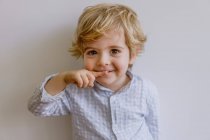 Criança adorável vestindo camisa casual sorrindo e olhando para a câmera no fundo branco do estúdio — Fotografia de Stock