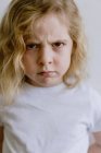 Розчарована маленька дитина в повсякденній футболці дивиться на камеру на білому тлі в студії — стокове фото