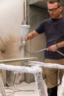 Focused workman using airbrush for applying flame retardant to wood detail ensuring fire protection in carpentry workshop — Stock Photo