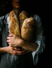 Cropped unrecognizable woman in apron holding ciabatta bread while standing on dark background — Stock Photo