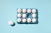 Eggs in paper tray and one on blue surface — Stock Photo
