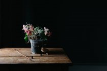 Composition de fleurs naturelles poussant en pot sur une table en bois minable dans une pièce sombre — Photo de stock