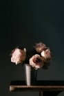 Квітучі свіжі рожеві троянди в старовинній вазі розміщені на дерев'яному столі на чорній стіні в сучасній квартирі — стокове фото